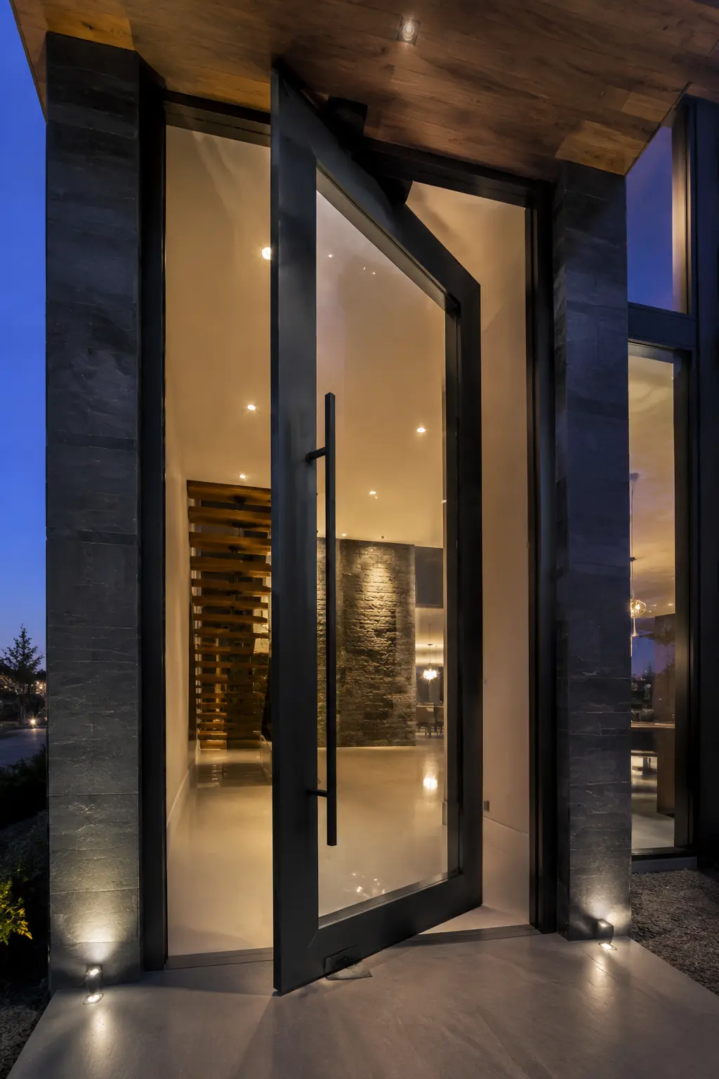 Oversized glass steel pivot door opening at blue hour